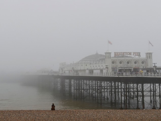 Mulher olha em direção ao pier envolto em névoa do mar na cidade de Brighton, no sul da Inglaterra - 13/04/2015
