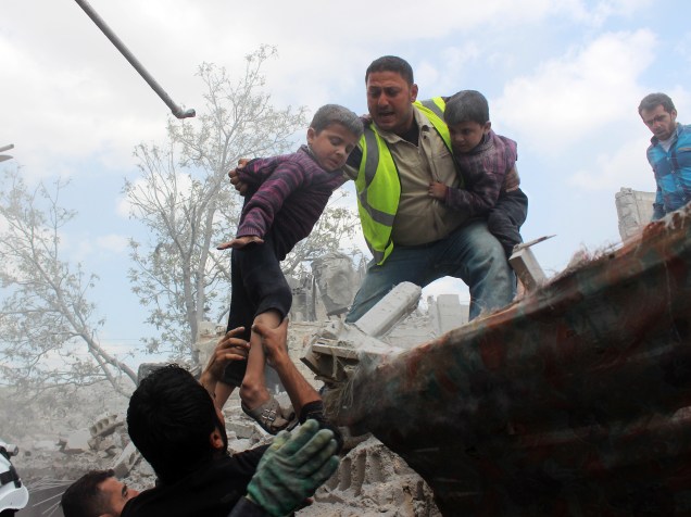Equipes de defesa civil evacuam crianças de um edifício na sequência de um ataque aéreo atribuído às forças do governo sírio em um território controlado por rebeldes no bairro residencial de Maadi em Aleppo - 14/04/2015