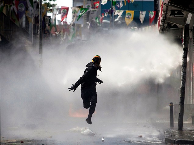 Manifestante mascarado foge do jato de um canhão de água durante confrontos com a polícia no bairro Okmeydani em Istambul, na Turquia - 01/05/2015