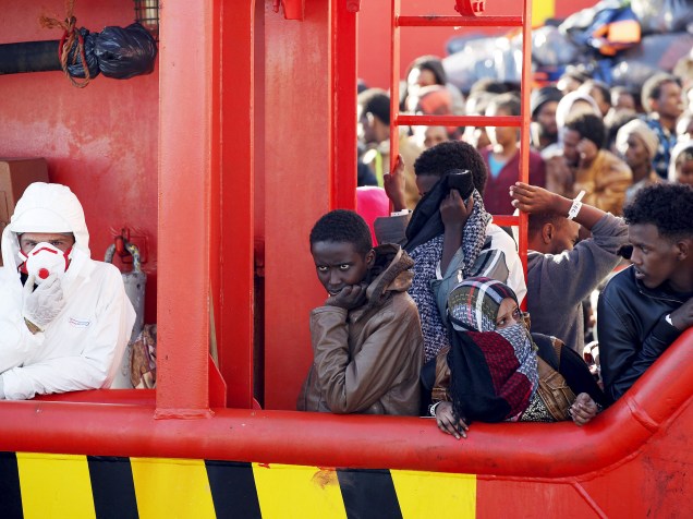 Acompanhados por um funcionário vestido com uniforme de proteção, imigrantes africanos aguardam para desembarcar do navio reboque Asso29 após serem resgatados do mar em porto siciliano de Pozzallo, na Itália - 04/05/2015