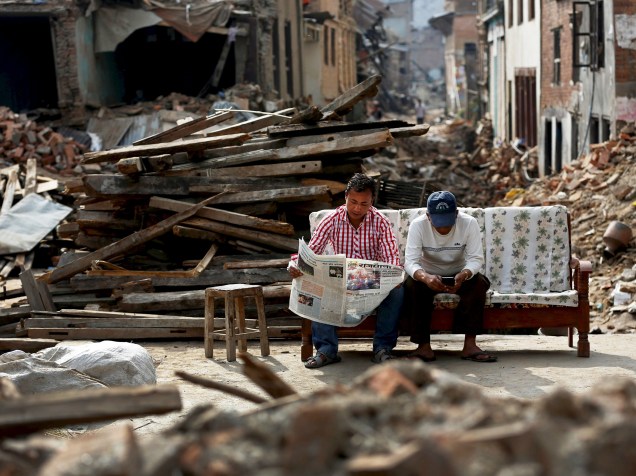 Homem lê jornal ao lado de seu amigo em meio aos escombros de casas destruídas nos arredores de Kathmandu, Nepal - 15/05/2015