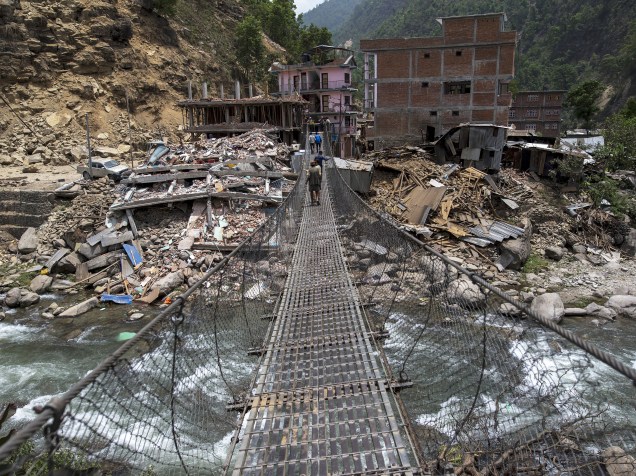 Moradores andam sobre uma ponte ligada a edifícios desmoronados após terremoto de terça-feira (12) na vila de Singati, em Dolakha, Nepal - 15/05/2015