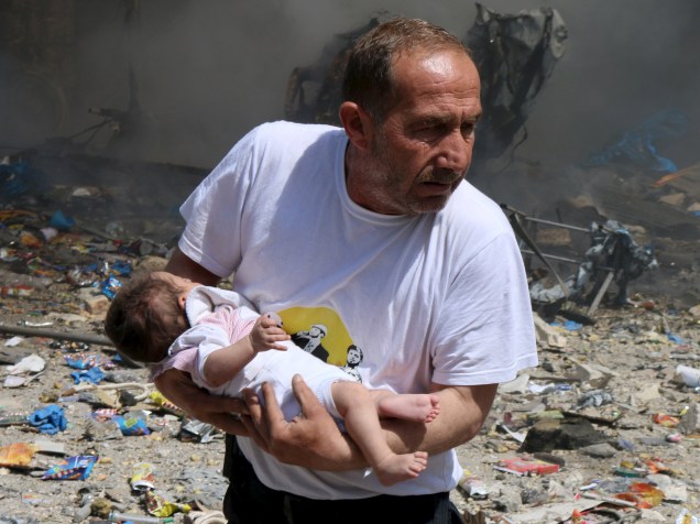 Homem carrega bebê que sobreviveu a explosão de bomba lançada por forças fiéis ao presidente da Síria, em Aleppo - 03/06/2015