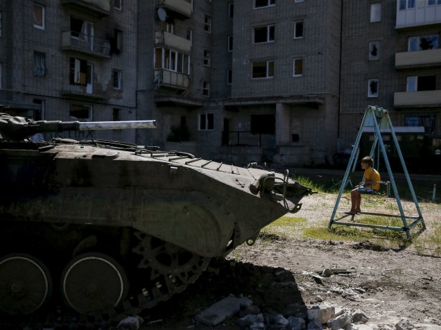 Menino senta-se em um balanço perto de seu prédio, danificado durante os combates entre o Exército ucraniano e separatistas pró-Rússia, na cidade Avdeyevka,  perto de Donetsk, leste da Ucrânia