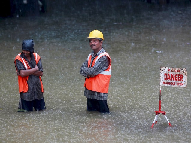 Trabalhadores em pé próximo a uma placa que sinaliza que a estrada está inundada devido às fortes chuvas que atingem Mumbai, Índia - 19/06/2015