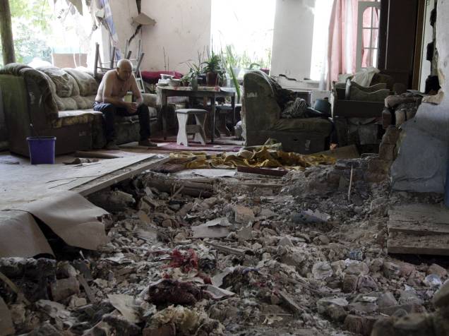 Morador senta em meio aos destroços de sua casa, que foi atingida por bombardeio em Donetsk, Ucrânia - 22/06/2015