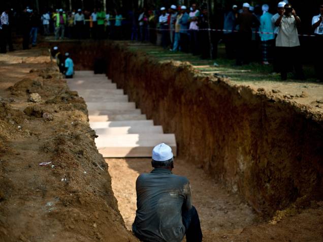 Muçulmano senta próximo a uma cova durante enterro dos restos mortais do que acreditam ser pessoas da etnia Rohingya encontradas em um acampamento de tráfico humano em Kampung Tualang. Autoridades da Malásia organizaram um funeral para os 21 corpos não identificados encontrados - 22/06/2015