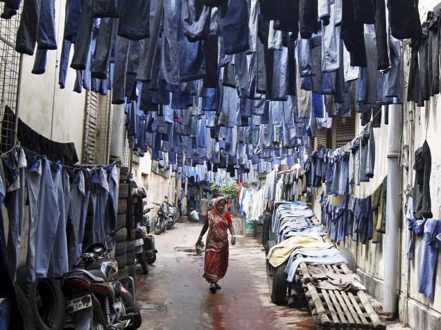 Mulher anda por um beco repleto de calças penduradas para secar antes de serem vendidas em um mercado de Calcutá, na Índia - 29/06/2015