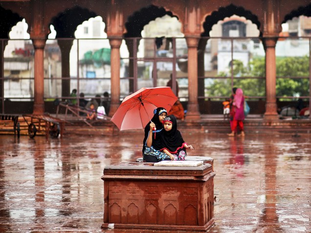 Meninas sentam-se sobre um móvel enquanto se protegem de forte chuva em Nova Délhi, na Índia - 10/07/2015