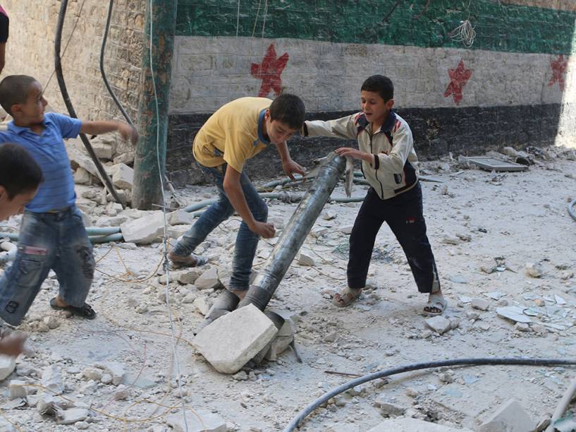 Meninos brincam com um cano fingindo ser um morteiro em local que, segundo ativistas, foi alvo de um bombardeio com barril de explosivos na cidade de Aleppo, na Síria, no domingo (12)