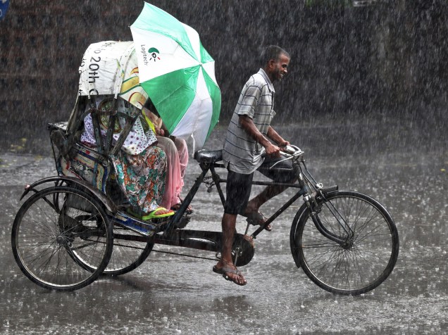 Em Chandigarh, na Índia, pessoas se protegem de chuva enquanto viajam em um riquexó - 20/07/2015
