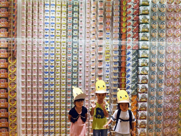 Crianças posam para foto em frente a um painel com pacotes de macarrão instantâneo de vários países no Museu Cup Noodle em Yokohama, no subúrbio de Tóquio