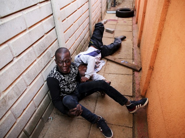 Suspeito se contorce de dor enquanto está algemado a seu cúmplice depois de ser baleado durante uma tentativa de invasão à casa de um casal de policiais, no sul de Johannesburgo, na África do Sul