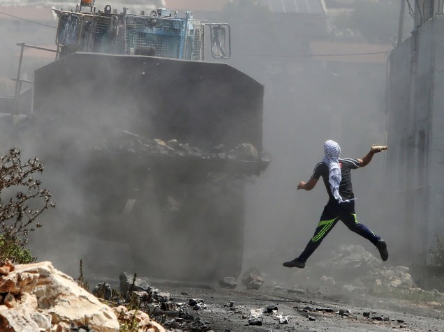 Manifestante palestino joga uma garrafa com tinta em uma escavadeira do exército israelense, durante confronto após protesto contra a expropriação da de terra Palestina por Israel - 21/08/2015