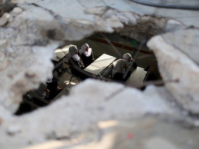Estudantes palestinas são fotografadas por um buraco no teto de uma sala de aula danificada por ataques liderados por Israel. Os ataques ocorreram durante a guerra que durou 50 dias e terminou em agosto do ano passado, em Khan Yunis, sul da Faixa de Gaza - 24/08/2015