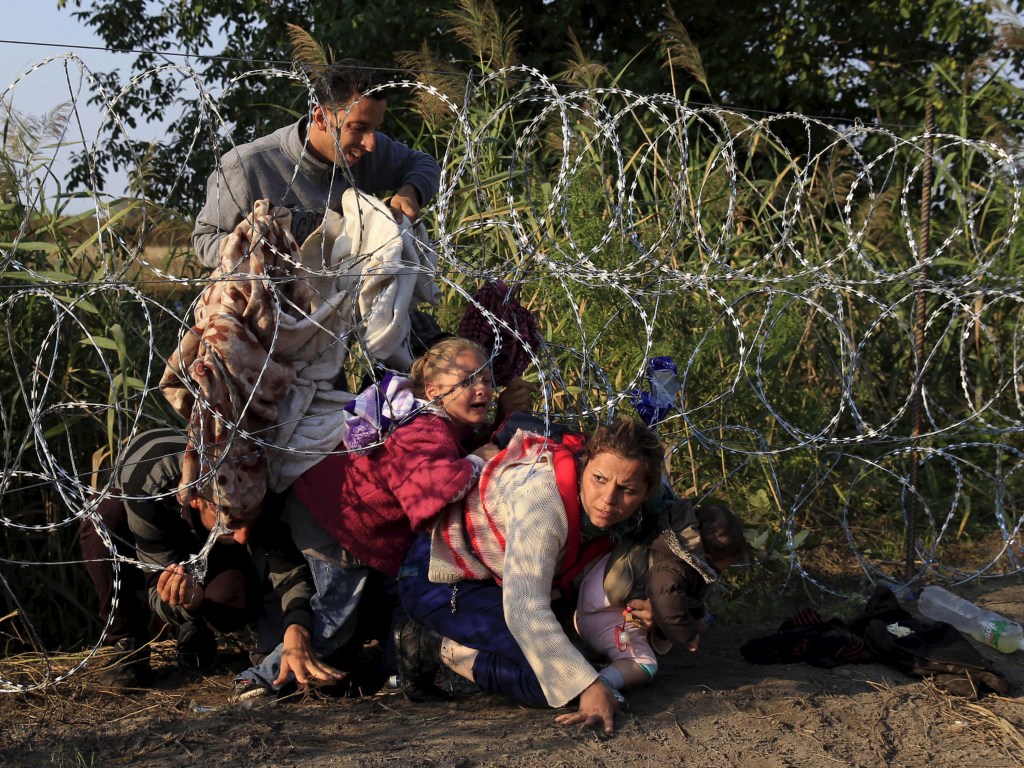 Imigrantes sírios tentar passar por baixo de cerca para entrar na Hungria, na fronteira com a Sérvia. A Hungria iniciou a construção de uma cerca de 175 km na região e planeja reforçar a segurança com helicópteros, polícia montada e cachorros - 27/08/2015