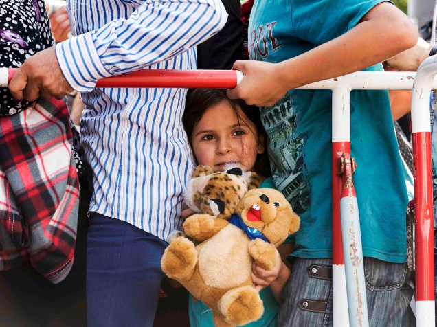 Menina refugiada leva seu urso de pelúcia enquanto tenta entrar em Munique, na Alemanha com sua família