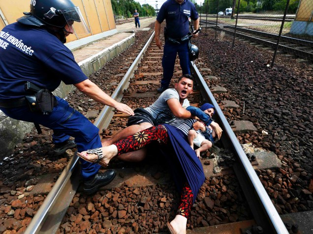 Família de refugiados se protege de policiais na estação ferroviária na cidade de Bicske, Hungria. A composição seguia para a fronteira com a Áustria.