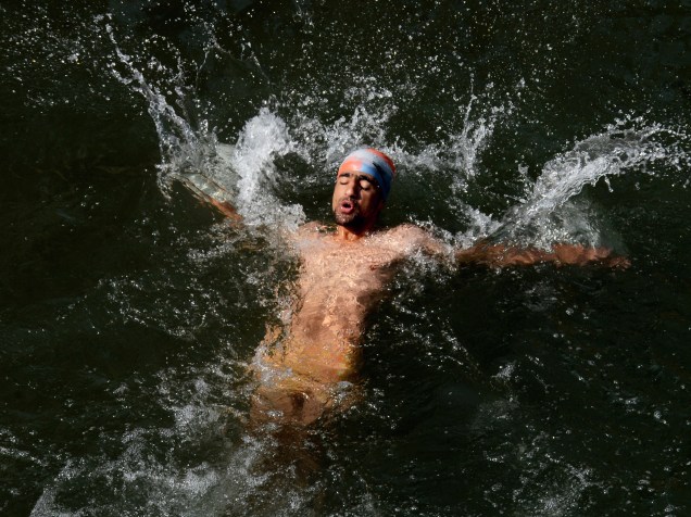 Homem nada em um córrego durante dia quente nos arredores de Srinagar, Índia