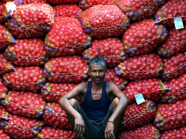 Trabalhador indiano descansando ao lado de sacos de cebolas num mercado de Allahabad