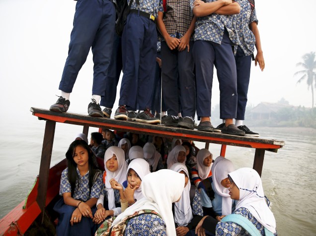Estudantes se equilibram no teto de um barco durante travessia do rio Musi rumo à escola em Palembang, Indonésia 10/09/2015