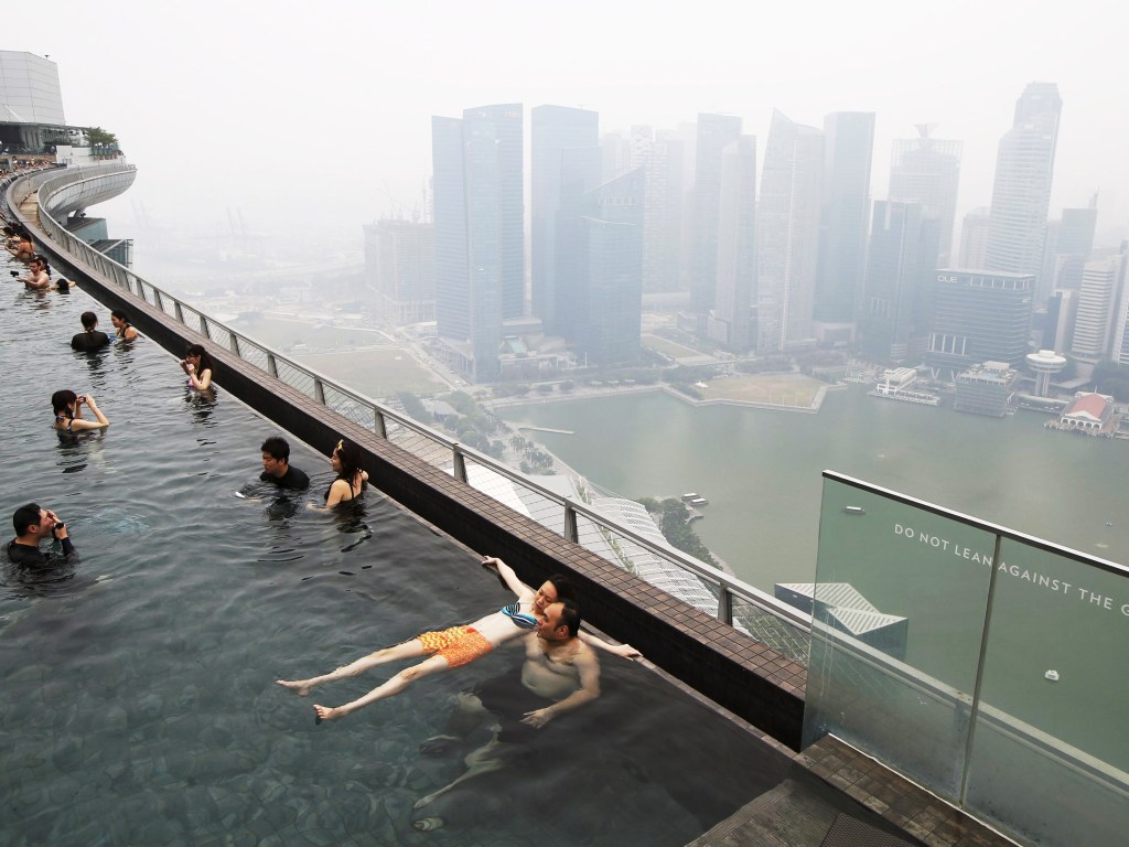 Pessoas nadam em uma piscina com vista para o skyline do distrito comercial em Singapura - 14/09/2015