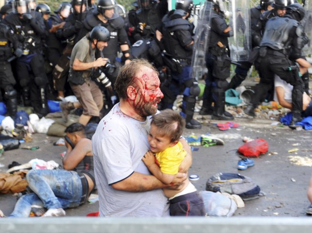 Homem ferido carrega uma criança durante confrontos entre refugiados e a polícia húngara na fronteira com a Sérvia em Röszke - 16/09/2015