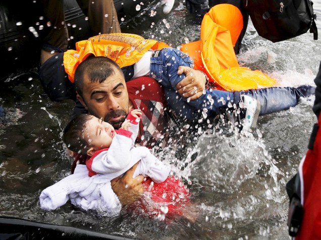 Refugiado sírio segura crianças enquanto se esforça para sair de um bote na ilha grega de Lesbos - 24/09/2015