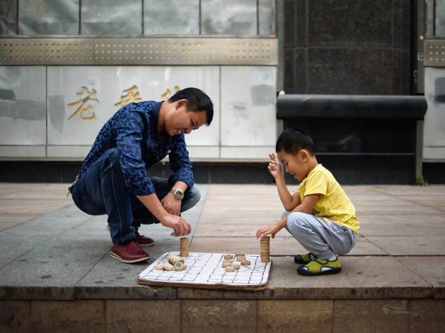 Um homem e um garoto são fotografados enquanto se divertem com jogo de tabuleiro em uma rua de Pequim, China - 06/10/2015