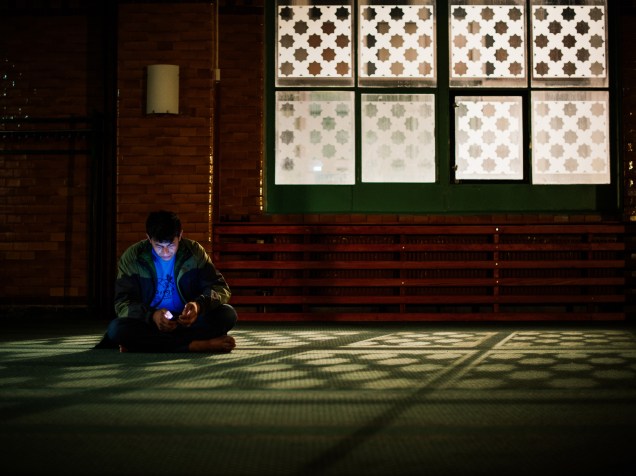 Refugiado verifica seu telefone na sala de oração da mesquita de Estocolmo, na Suécia