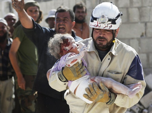 Bombeiro da Defesa Civil carrega um bebê ferido que sobreviveu após ficar soterrado em um local atingido por um ataque aéreo de forças leais ao ditador sírio Bashar Assad, na cidade de Marshamsha, sul da Síria