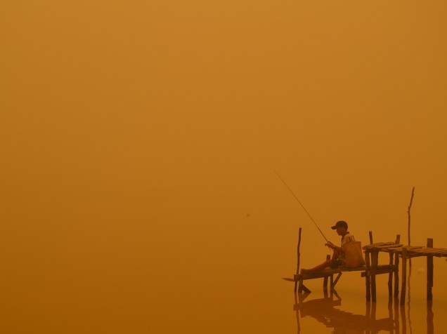 Pescador foi fotografado em meio a névoa ácida à beira de um rio na cidade de Palangkaraya, na Indonésia; incêndios florestais e agrícolas cobrem o sudeste da Ásia com uma nuvem