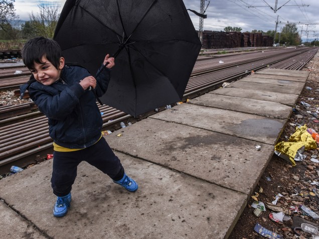 Criança segura um guarda-chuva enquanto espera por um trem com outros refugiados depois de cruzar a fronteira da Macedônia com a Sérvia perto da cidade de Bujanovac - 23/10/2015