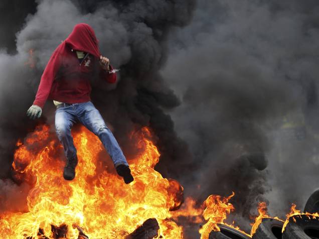 Manifestante palestino salta sobre pneus em chamas durante confronto com tropas israelenses perto do assentamento judaico de Bet El, nos arredores da cidade de Ramallah, na Cisjordânia - 26/10/2015