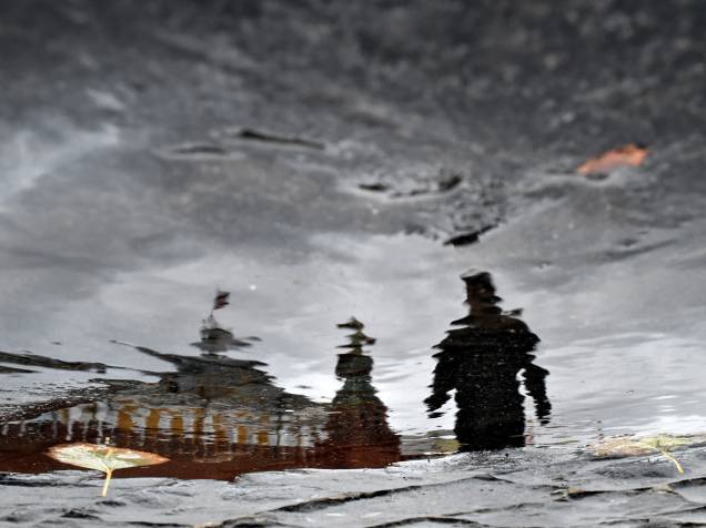 Um homem é refletido em uma poça dágua enquanto caminha pela Praça Vermelha, em Moscou