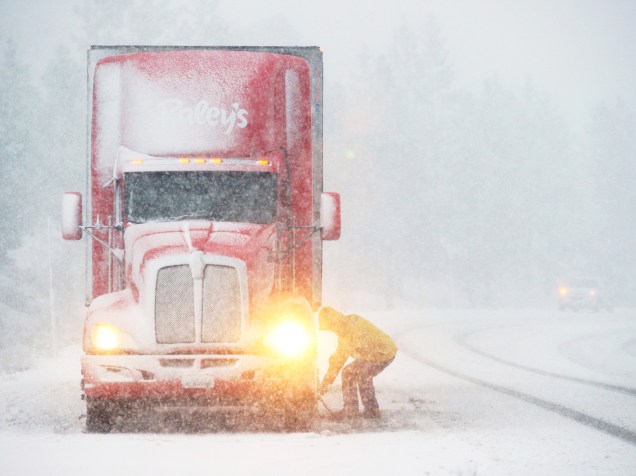 Motorista instala correntes nas rodas de seu caminhão, durante nevasca na estrada de Woodford, Califórnia - 25/11/2015