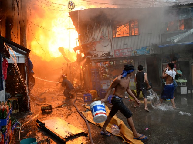 Bombeiro conta com a ajuda de moradores para apagar um incêndio em uma favela próxima a uma prisão em Manila, nas Filipinas. Centenas de presos foram evacuados e milhares de pessoas ficaram desabrigadas - 04/12/2015