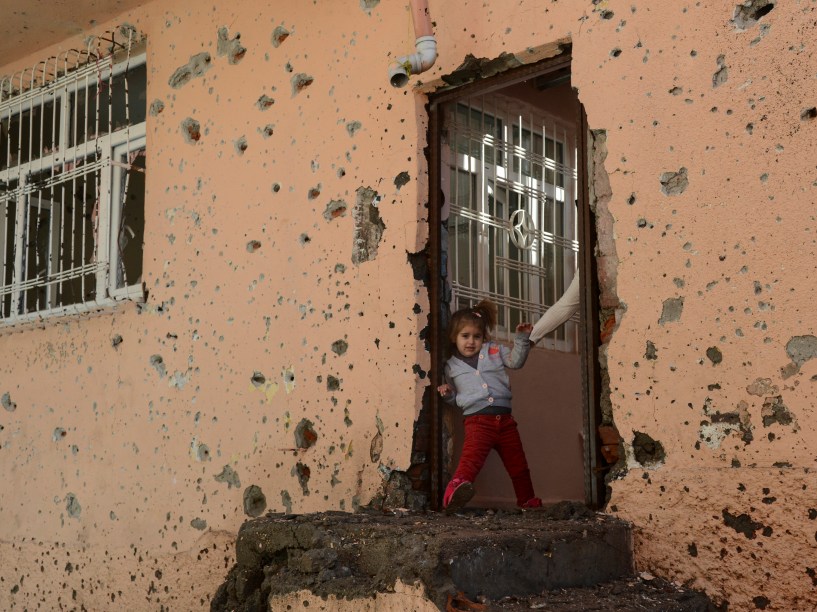 Menina fica na entrada de uma casa danificada no distrito de Sur em Diyarbakir, na Turquia. Um policial foi morto por um atirador enquanto tentava desarmar um artefato explosivo no local - 11/12/2015