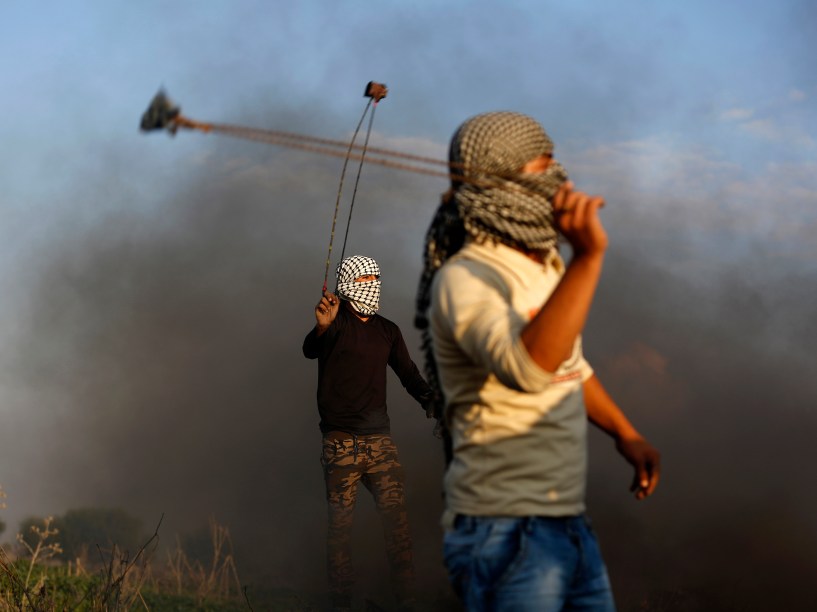 Manifestantes palestinos usam estilingues para lançar pedras em direção às forças de segurança israelenses durante confronto ao longo da cerca da fronteira com Israel na periferia da Cidade de Gaza - 11/12/2015