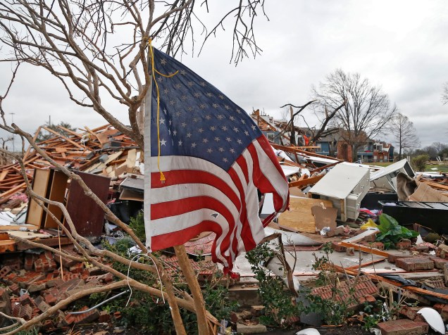 Bandeira esfarrapada dos Estados Unidos é colocada sobre os galhos de uma árvore em meio aos escombros das casas da cidade de Garland no Texas, após passagem de um tornado no último sábado (26)