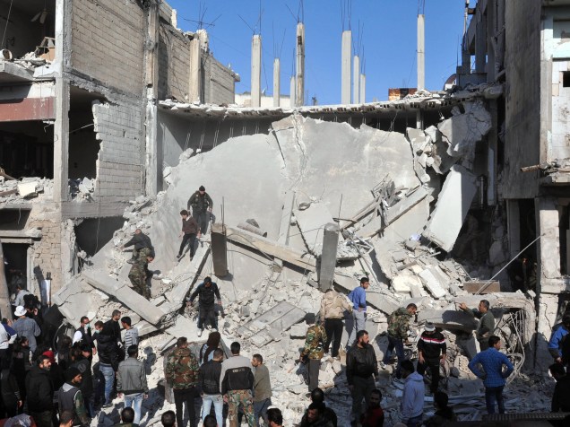 Sírios analisam os escombros no distrito de Al Zahra, na cidade síria de Homs, onde foi registrado um ataque duplo contra a população - 28/12/2015
