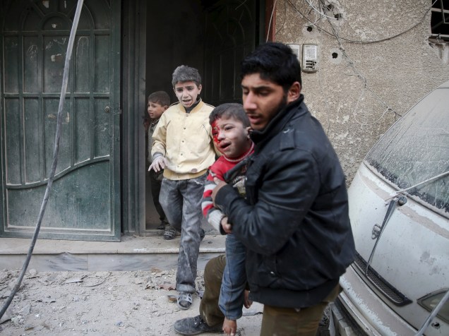 Homem carrega criança ferida durante ataque de forças leais ao presidente da Síria, Bashar al-Assad, na cidade de Douma - 30/12/2015