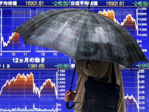 Um pedestre segurando um guarda-chuva observa telão mostrando a variação da Bolsa de Tóquio em uma rua da capital japonesa, após o impacto da notícia com o pior resultado da economia da China em 25 anos