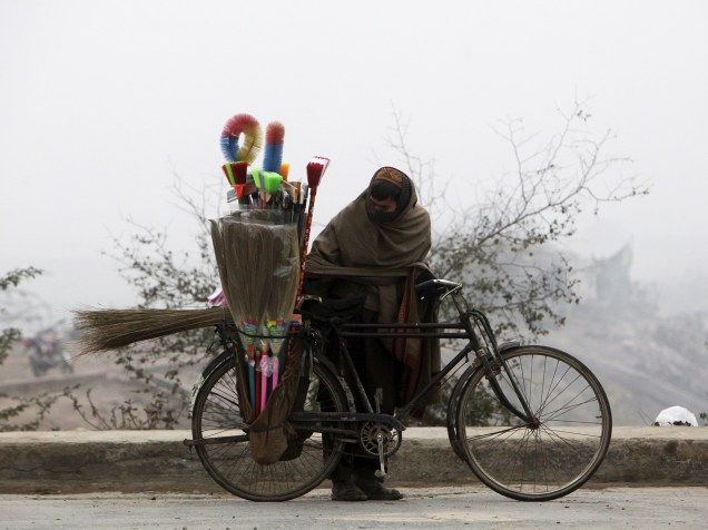 Vendedor de escovas tenta se proteger do frio em Lahore, no Paquistão
