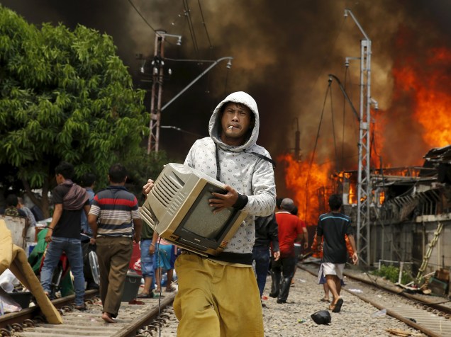 Moradores de uma favela carregam seus pertences durante um incêndio ao lado de uma ferrovia em Kampung Bandan, na Indonésia