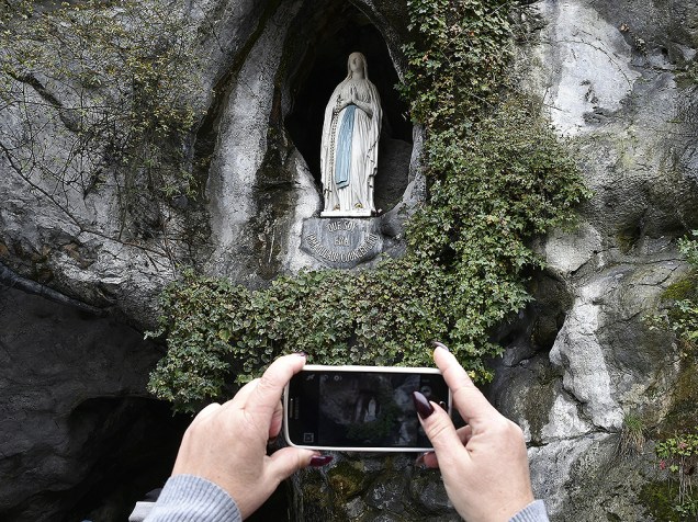 Peregrino faz uma fotografia da estátua da Virgem Maria, dentro da gruta de Massabielle, no sul da França