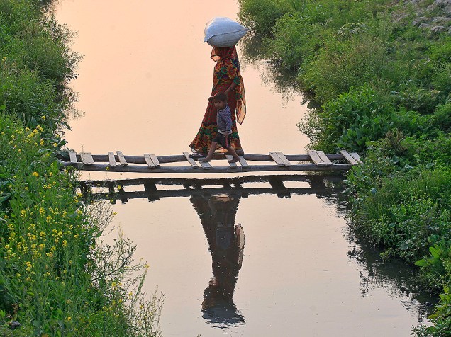 Mulher dá sua mão para um garoto, ao atravessar uma ponte improvisada feita de bambu, em um canal, na cidade de Allahabad, na Índia