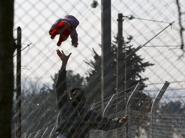 Imigrante joga seu bebê para o ar, enquanto espera para entrar na Macedônia