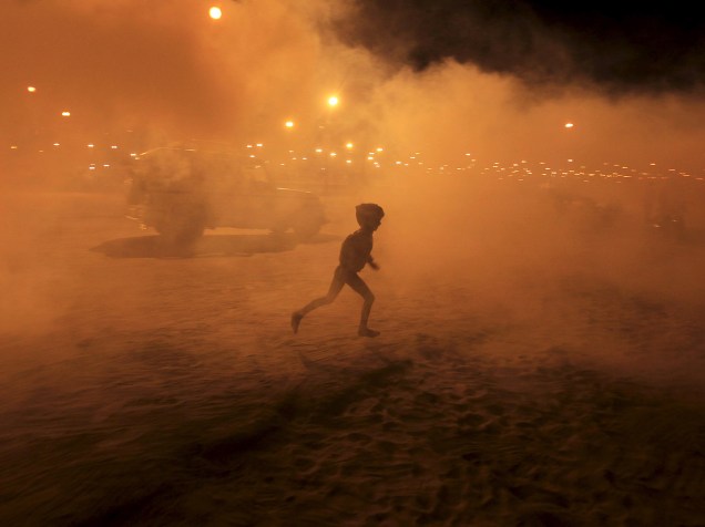 Garoto corre em meio à fumaça de fumigação, feita pelos profissionais de saúde, às margens do Rio Ganges, na cidade de Allahabad, na Índia