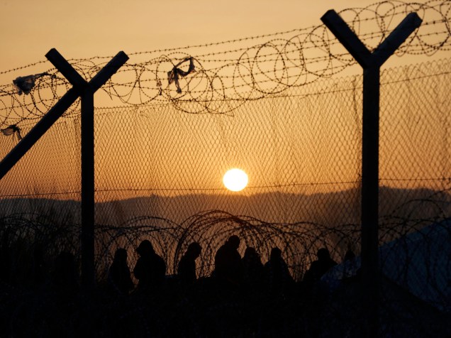 Refugiados aguardam atrás de uma cerca na fronteira entre Grécia e Macedônia, nesta terça-feira (23), após as restrições de passagem adicionais impostas pelas autoridades macedónias deixou centenas de presos perto da aldeia de Idomeni, na Grécia
